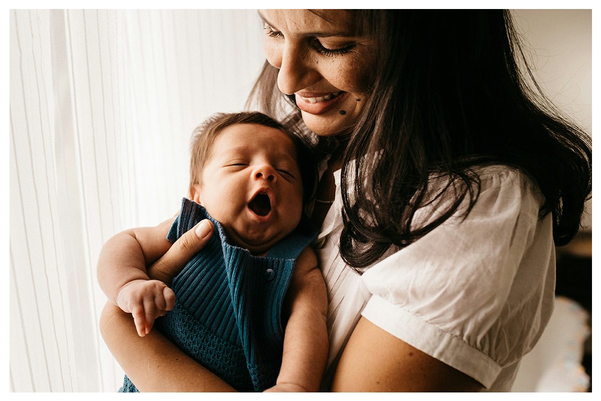 Mother smiling while holding her yawning newborn at home